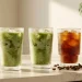 A row of ribbed glassware filled with iced matcha and cold brew on a sunny kitchen counter.